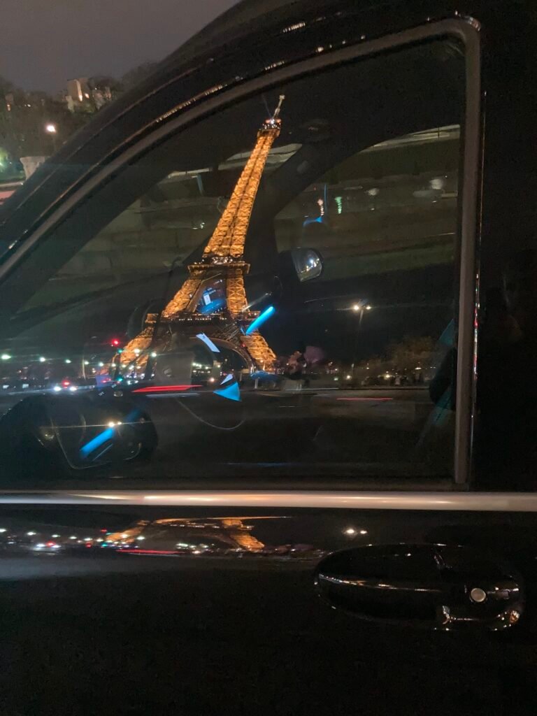Guide vtc paris : Tour Eiffel illuminée reflétée dans la vitre d'un véhicule de chauffeur privé à Paris